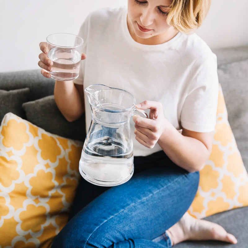 Vrouw schenkt thuis gefilterd water uit een karaf in een glas