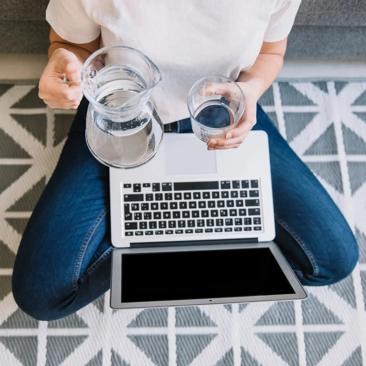 Persoon met laptop, een karaf gefilterd water en een glas water thuis