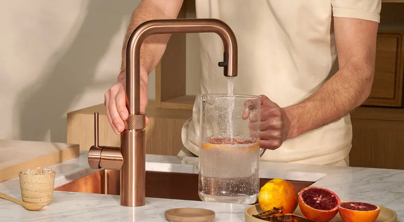 Quooker kokendwaterkraan in messing schenkt kokend water in een glazen theepot met verse munt in een sfeervolle keuken
