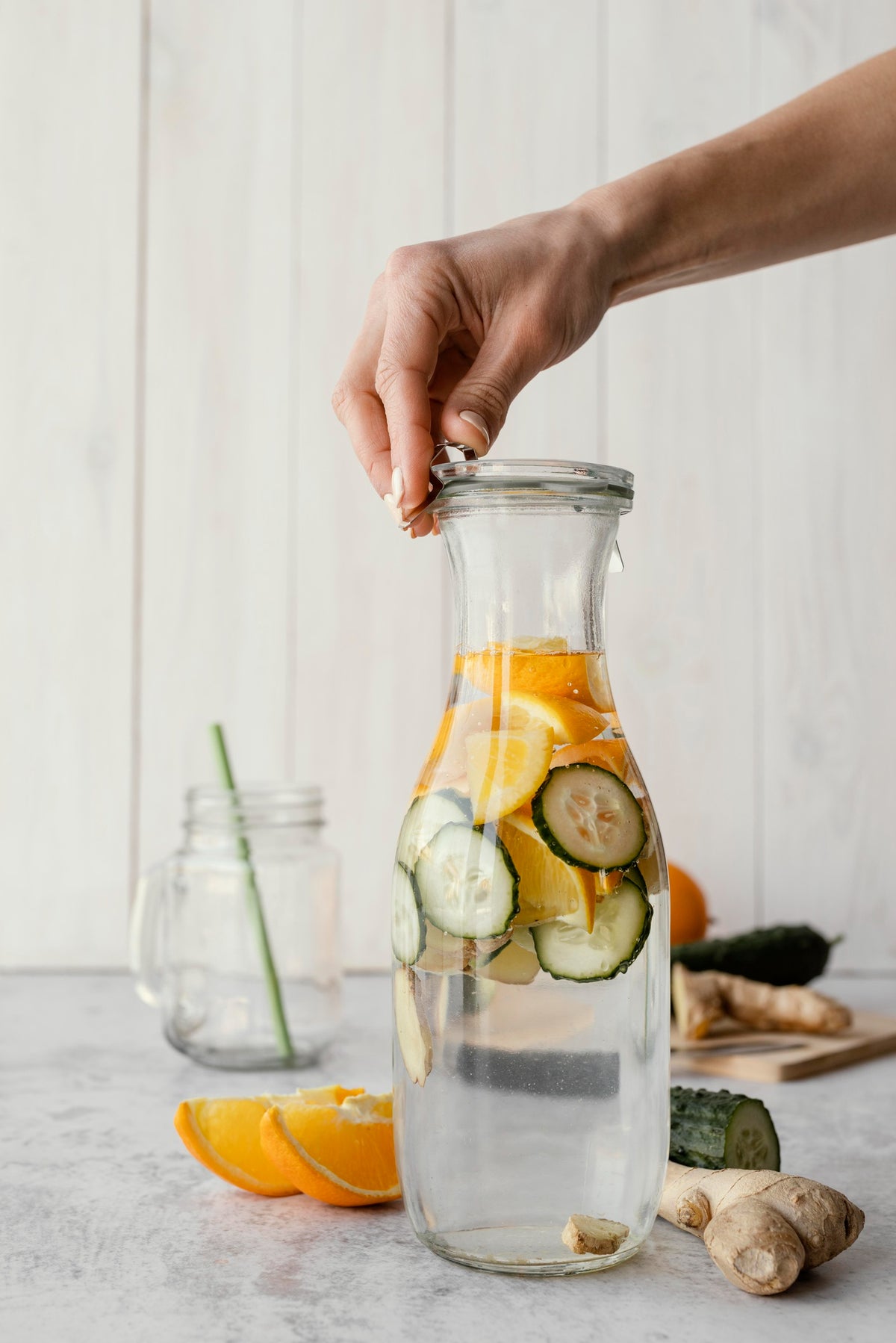 Glazen karaf met gefilterd water, schijfjes citroen, sinaasappel, komkommer en gember op een licht aanrecht