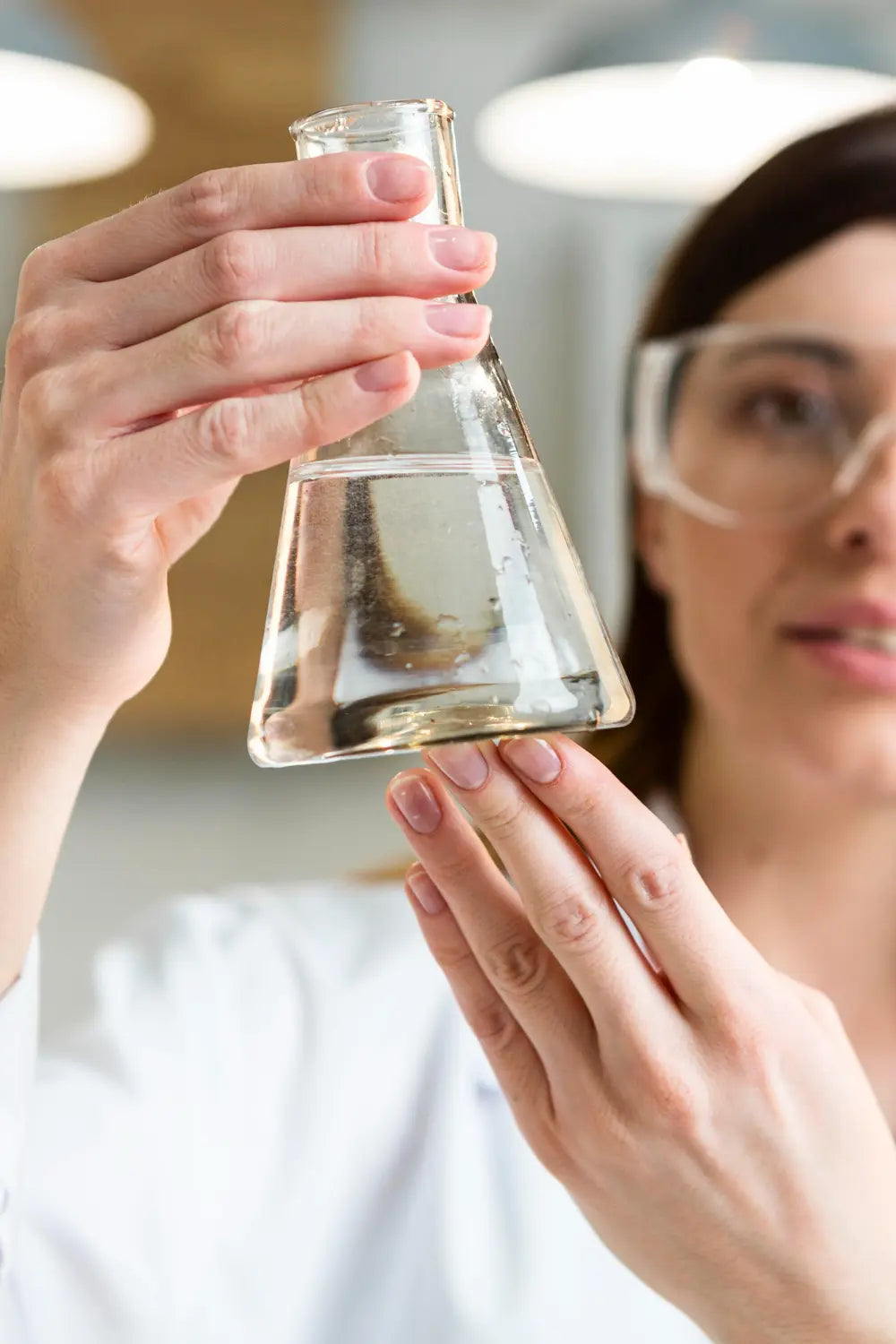 Laborante met veiligheidsbril inspecteert een watermonster in een erlenmeyer om de waterkwaliteit te beoordelen